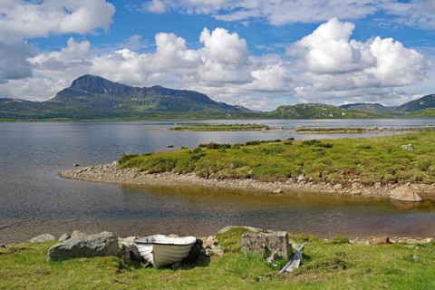 Lake with a small boat on the shore surrounded by green mountains under blue sky, Bygdin,