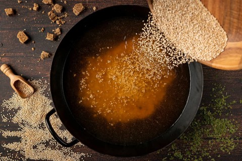 Quinoa is poured into a pan of broth surrounded by spices on a rustic wooden table
