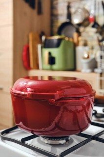 Red cooking pot on gas stove in modern kitchen. Background shows various kitchen tools and green