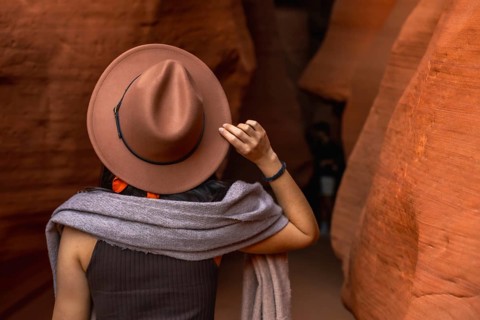Woman wearing a hat and scarf exploring the narrow, winding sandstone walls of antelope canyon,