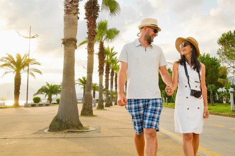 Young couple tourists walking hand in hand along Batumi promenade with palm trees and seaside view