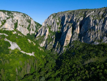 Majestic cliffs rise above a green forest under a bright blue sky, aerial view, Cheile Turzii,