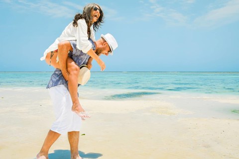 Multi-ethnic happy couple having fun piggyback riding on white sand beach. Caucasian man and middle