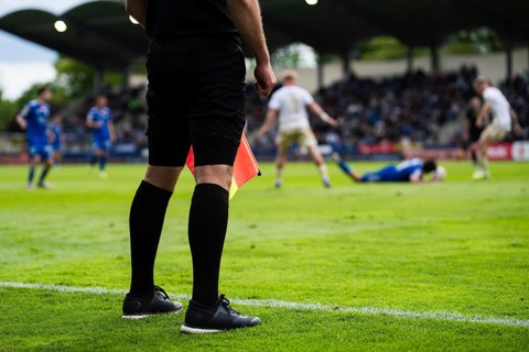 Assistant referee standing on the touchline during a football match, watching play unfold in a