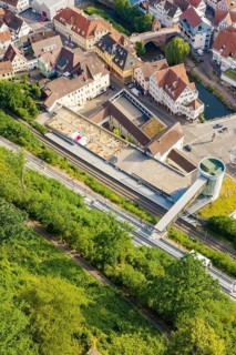 A train station with rails and buildings surrounded by green vegetation in summer,
