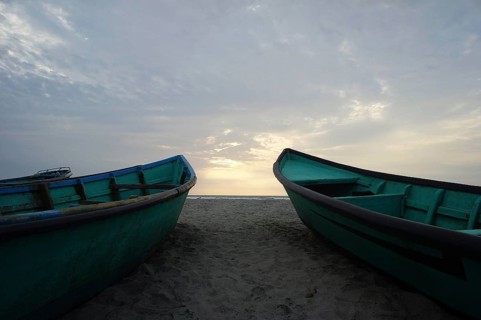 Two boats are lying, turquoise, next to each other on the beach, with a view of the sunset over the