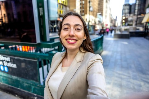 Young woman smiling and looking at the camera, dressed in business casual attire in front of a