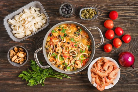 Seafood saute with tomatoes and black olives on a wooden table. Fresh shrimp, squid rings and