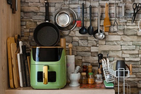 Kitchen counter with air fryer and various cooking tools like pans and utensils. Bright light