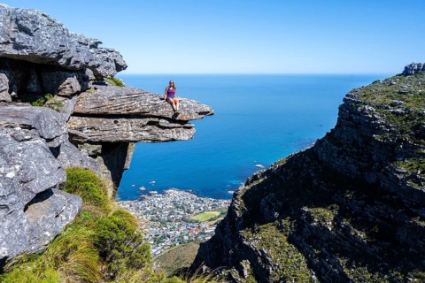 Young woman sitting on an imposing rock pin on a cliff, view of sea and coast, Kasteelspoort