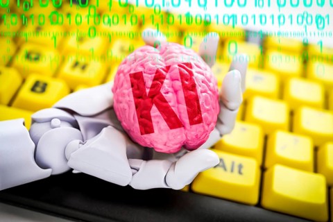 Robot hand holds a brain with the inscription AI in front of a computer keyboard, symbolic photo