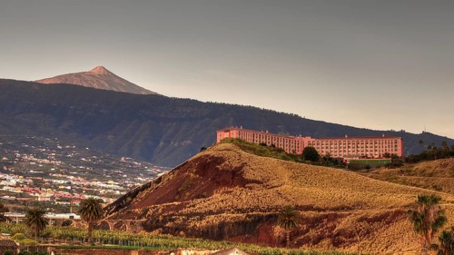 Puerto de la Cruz, large building on the slope of a mountain during golden hour, volcano in the