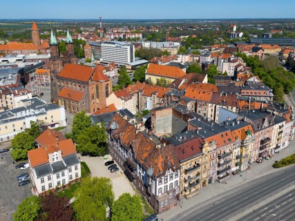 Aerial view of a historic town with red roofs and brick buildings, surrounded by green trees and
