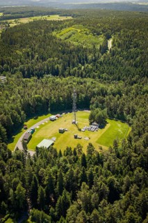 Radio tower in the middle of a forest, surrounded by green fields and trees from a bird's eye view,
