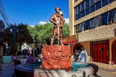 Bronze statue of a worker on a well in a busy urban environment with a modern building and