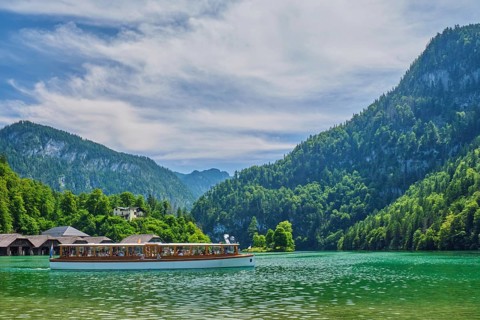 Side view of a white electric passenger boat cruising the emerald Konigsee lake under a dramatic