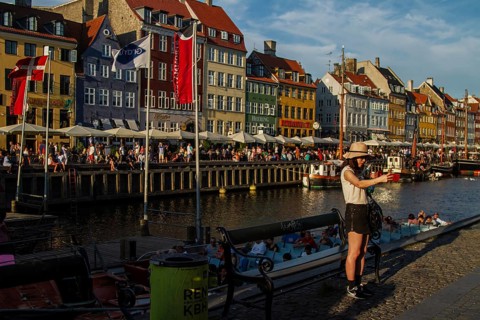 Frau mit Hut fotografiert an einem Wasserkanal vor bunten Häusern bei sonnigem Wetter, Kopenhagen