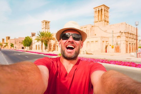 Happy male tourist wear red shirt and straw hat pose takes selfie at the Al Fahidi Historical