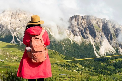 Woman hiker tourist by wooden safety railing fence by mist covered Seceda mountain peaks. Steep