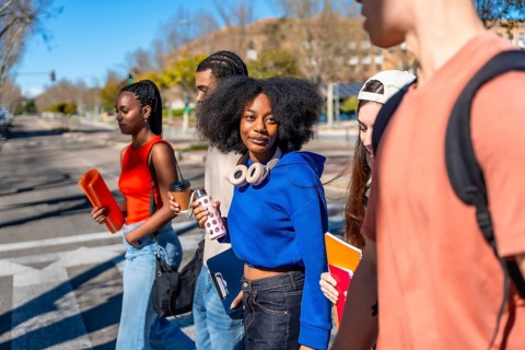 Group of multi ethnic students walking on a sunny university campus, carrying books, folders,