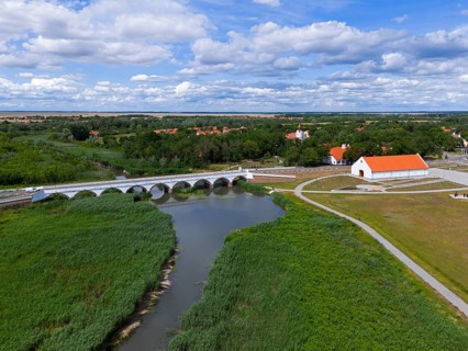 Landscape with a river, a bridge and a village surrounded by green meadows under a blue sky with