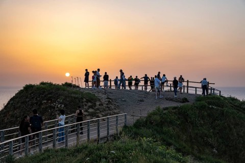 Tourists stand on the observation deck of the Falaise d'Aval rock formation and tourist attraction