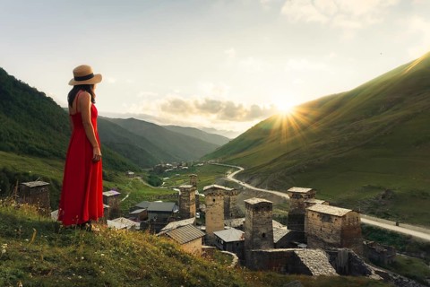 Young pretty Woman traveler in red dress looking at medieval towers of Ushguli Georgia during