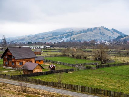 Wooden house with fenced meadows, hills in fog behind, Moldova, Romania