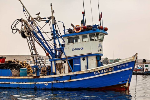 Close-up of a blue fishing boat with nets and ropes, in front of a harbor, fishing trawler in the