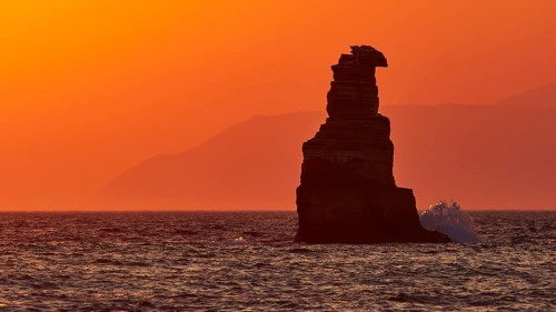 Rock formation in the sea against an intense orange sky during sunset, south of the Amari Basin,