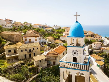 Aerial St. Spyridon Church in Dhrmi. White stone Orthodox chapel with blue domes overlooks Ionian