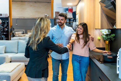 Young couple shakes hands with a sales consultant in a modern kitchen showroom, smiling as they