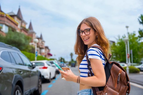 Young woman wearing glasses. A striped top. And a backpack. Walking on a city street while holding
