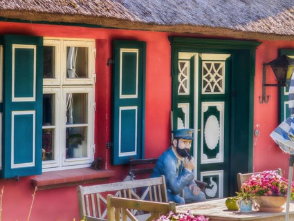 Thatched-roof house colorful door and window with sailor on bench Darß Baltic Sea Germany