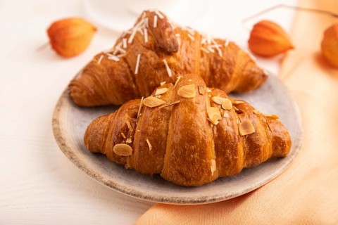 Croissant on blue plate on white wooden background and orange linen textile, cup of coffee, side