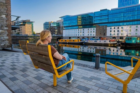 Woman relaxing on waterside benches surrounded by modern architecture and canal boats, Dublin,
