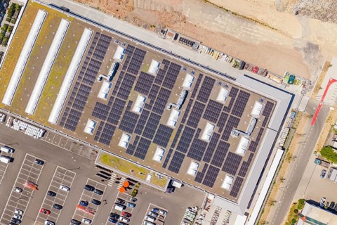 Aerial view of a large building with solar systems on the roof and parking spaces, PV system at OBI