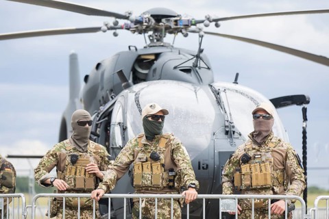 Masked pilots standing in front of a combat helicopter at the ILA (International Aerospace