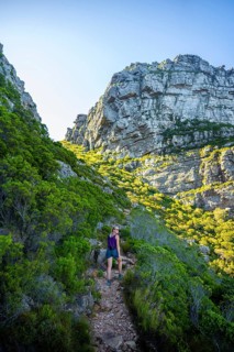 Kasteelspoort hiking trail, young woman hiking on a trail through a rocky, green landscape under