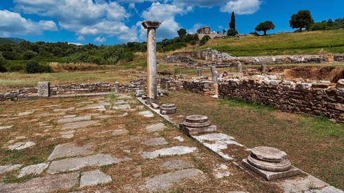 Ancient ruins with isolated stone columns in green landscape under blue sky, ancient site,