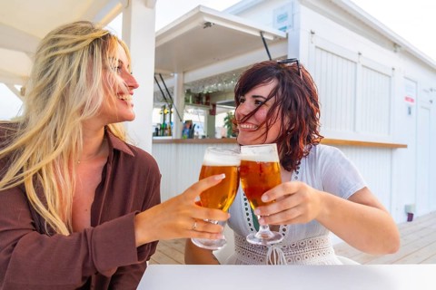 Two happy young women smiling, clinking glasses of refreshing beer, and celebrating friendship