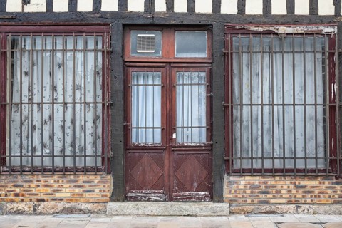 Weathered wooden entrance door to a historic half-timbered house with bars outside the windows in