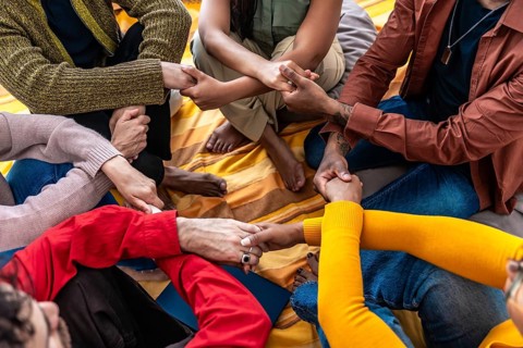 Diverse people sitting together in a close circle, holding hands and showing support, unity,