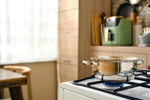 A pot on a gas stove with a blue flame underneath it. Natural light comes through a window in the