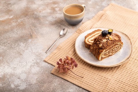 Sweet loaf with cream and caramel, cup of coffee, on brown concrete background with linen beige