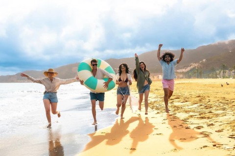 Diverse group of young adult friends running barefoot along the wet sand and shallow ocean waves,