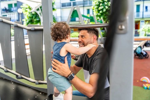 Enthusiastic father bonding with his happy toddler son at a vibrant park playground, sharing a