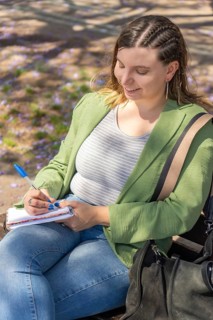 A cheerful young woman with braided hair, captured from a top-down angle, writing in a notebook
