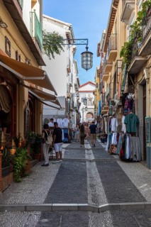 Lively shopping street with people between historic buildings under a blue sky, Granada