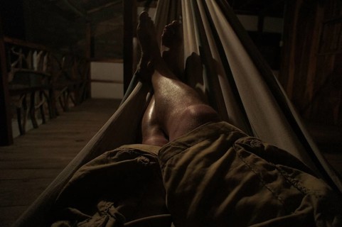 Person relaxing in a hammock on a dark wooden veranda, Ecuador